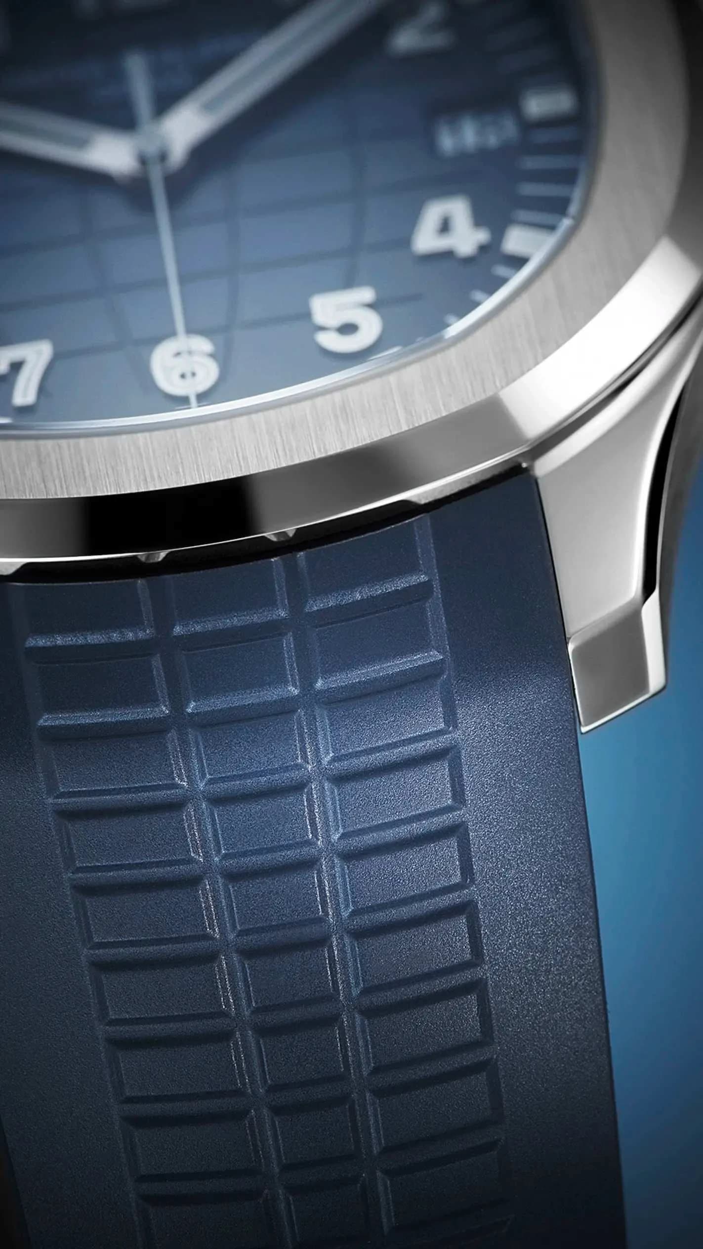 macro del borde de la caja y la unión con el brazalete de un reloj de esfera azul con índices arábigos luminiscentes y ventana de fecha, junto a una correa azul de goma con textura de cuadrícula