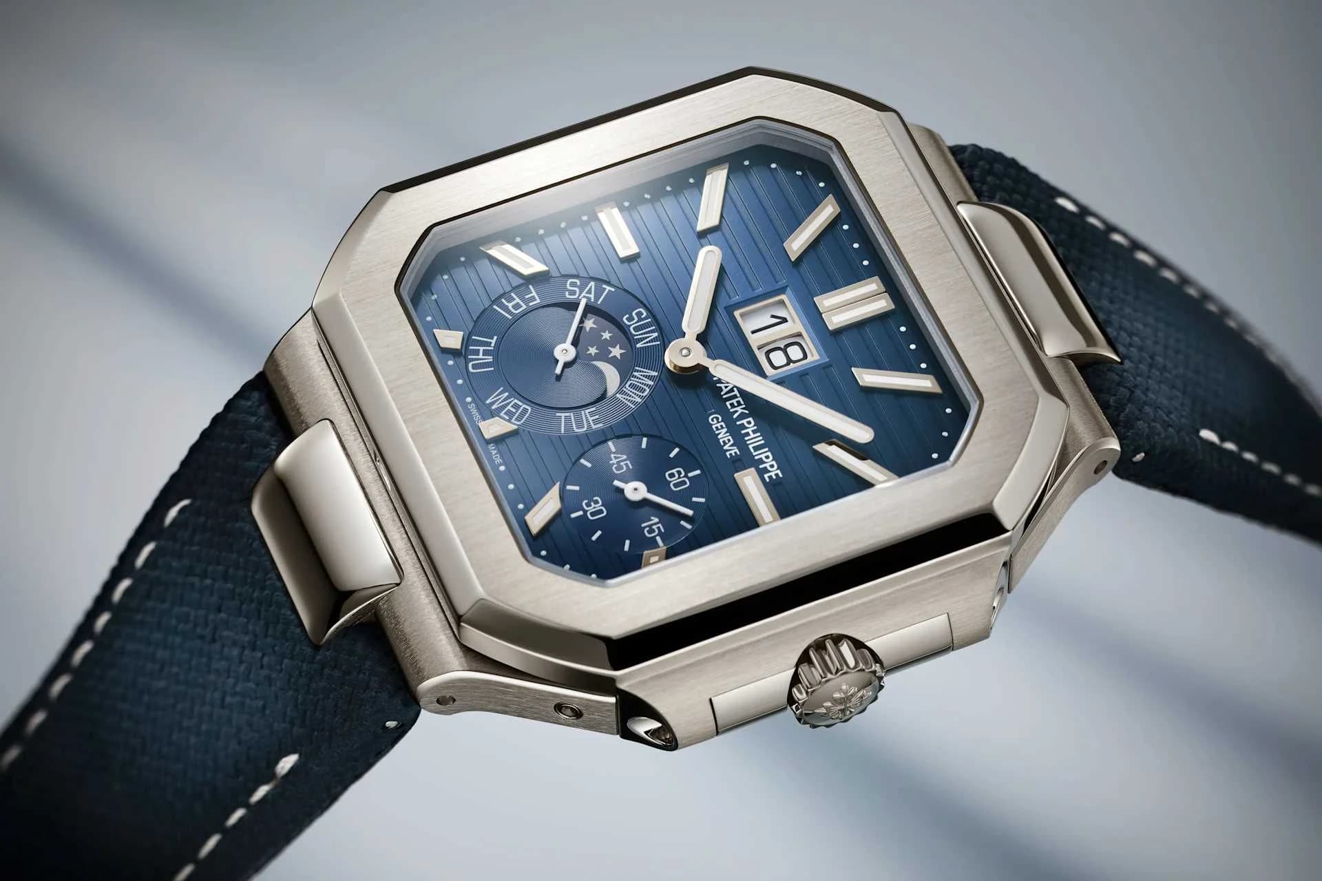 reloj Patek Philippe Geneve de caja octogonal en metal plateado con esfera azul con textura rayada, indicador de día de la semana, fase lunar, calendario de fecha grande y contador de minutos, sobre correa textil azul con costuras blancas