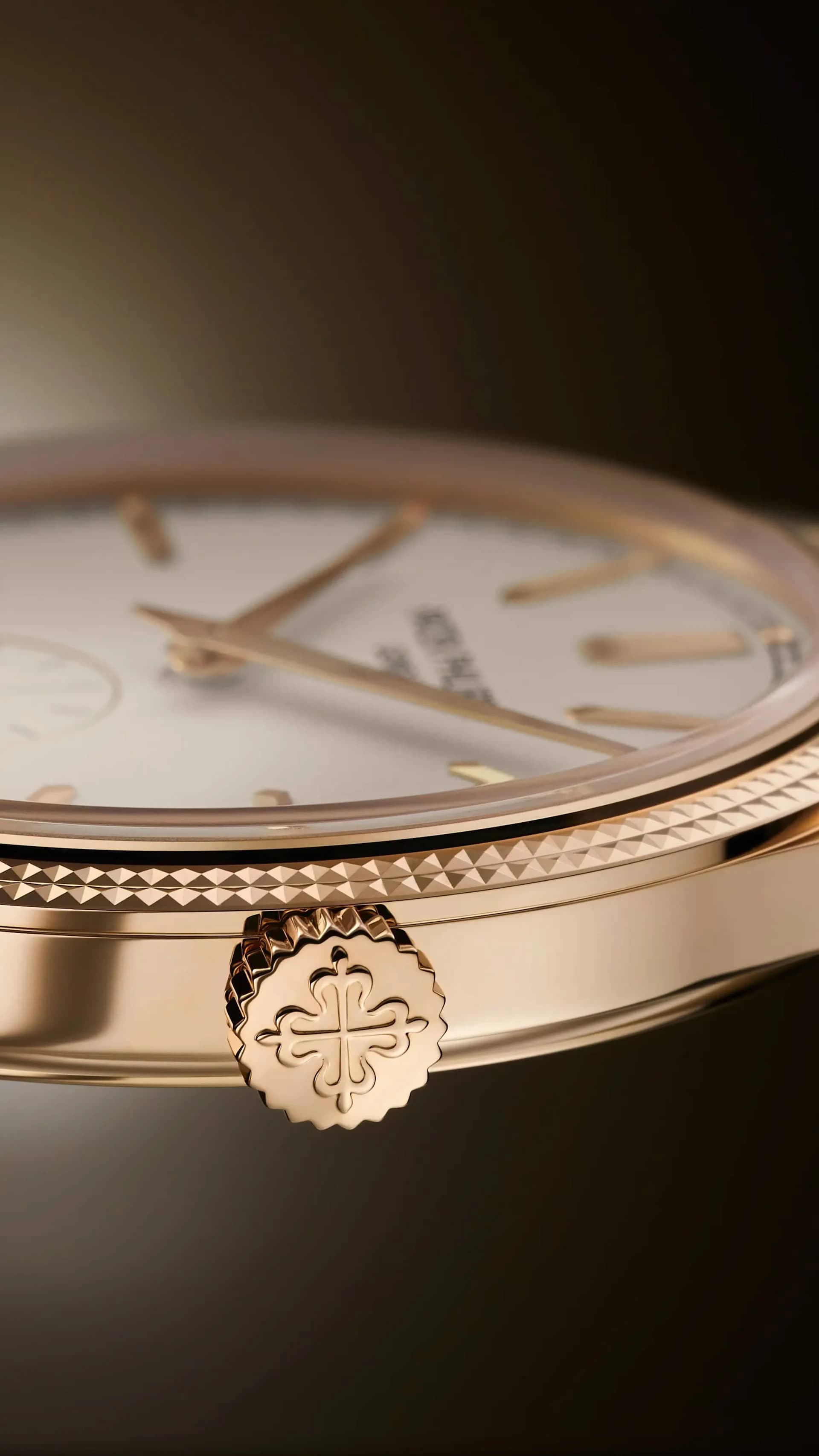 macro de la corona con cruz calada de un reloj dorado, junto al bisel decorado con motivo clou de paris y la esfera blanca vista de canto