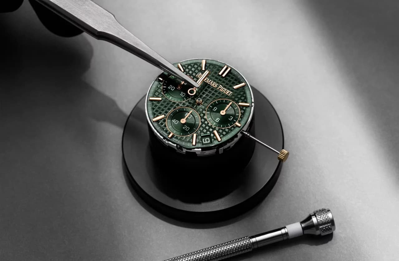 esfera verde con motivo de tapiz y tres contadores de cronógrafo de un reloj Audemars Piguet siendo manipulada con unas pinzas durante su montaje
