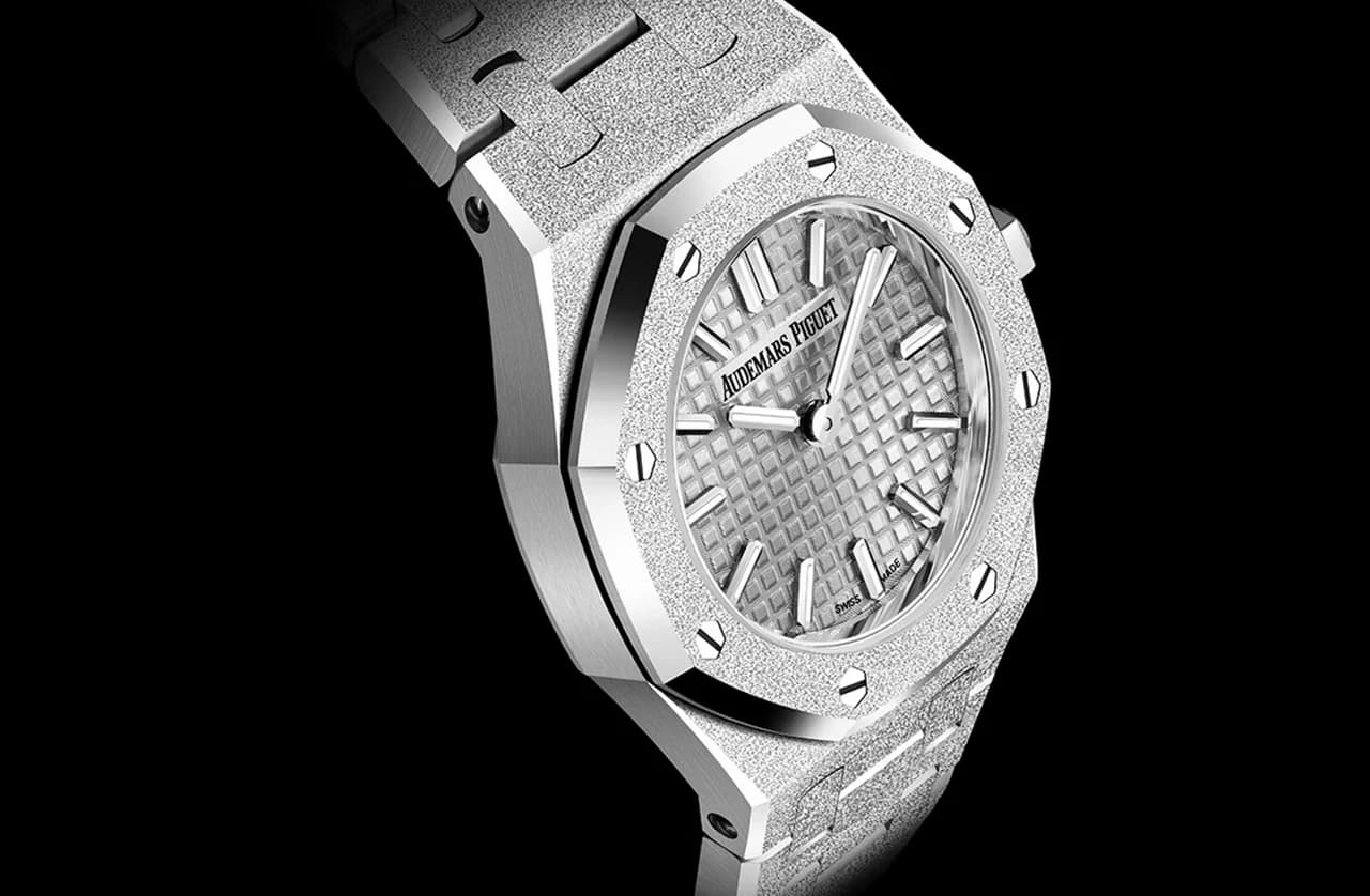 reloj octogonal con acabado escarchado, bisel de ocho tornillos visibles y esfera texturizada en patrón de cuadrícula con índices en forma de barra sobre fondo negro