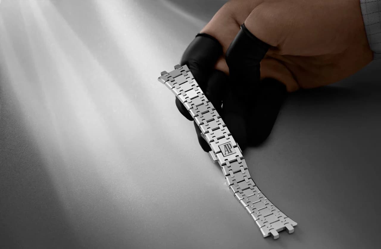 mano con guante negro sosteniendo un brazalete de eslabones de acero con cierre grabado con las iniciales AP